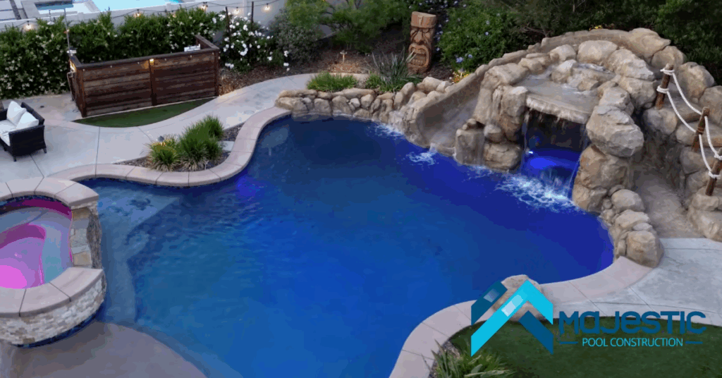 Custom freeform backyard pool in Southern California with rock waterfall, grotto, slide, spa, LED pool lighting, and travertine deck built by Majestic Pool Construction. representing freeform pools