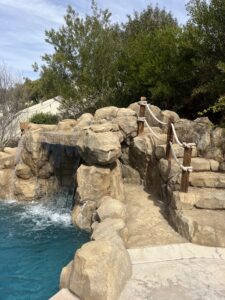 Rock waterfall with rope railing beside pool steps