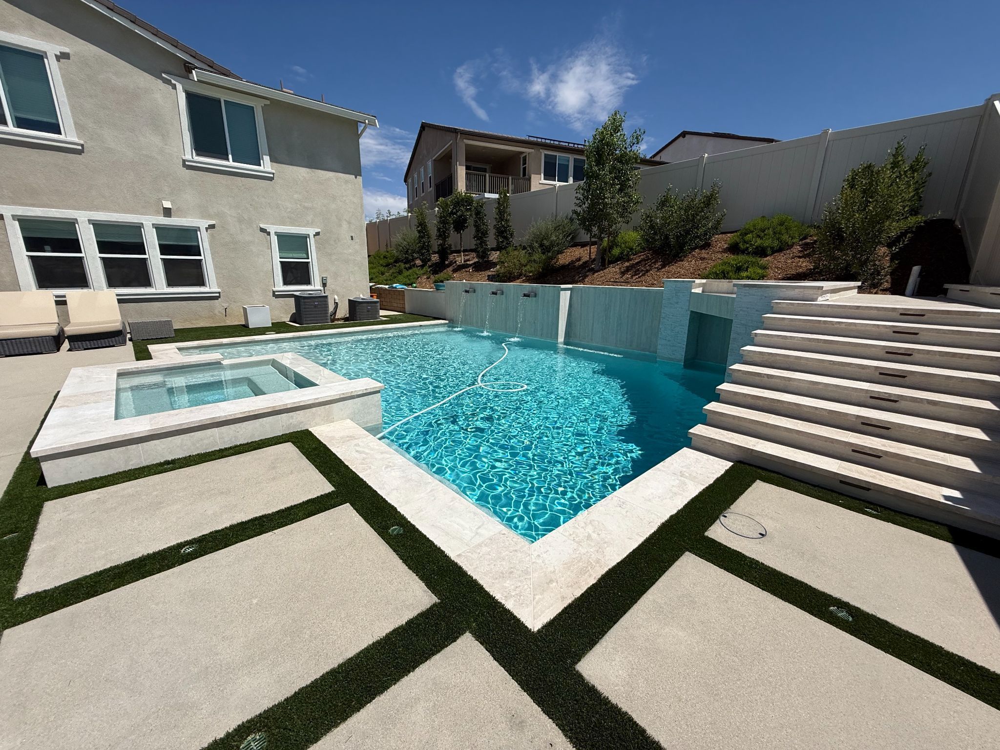 Modern backyard pool with spa, steps, and water features