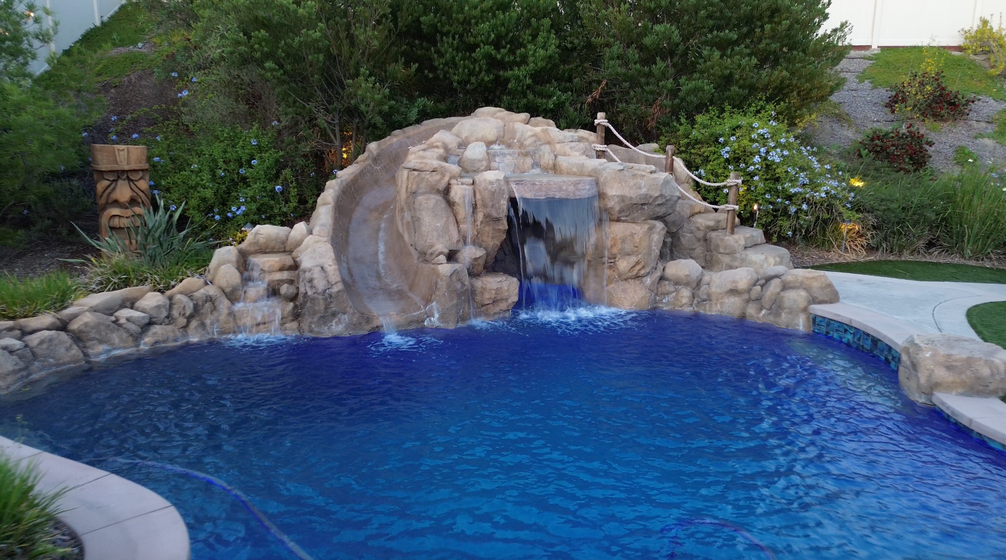 Rock waterfall pool with slide and tropical landscaping