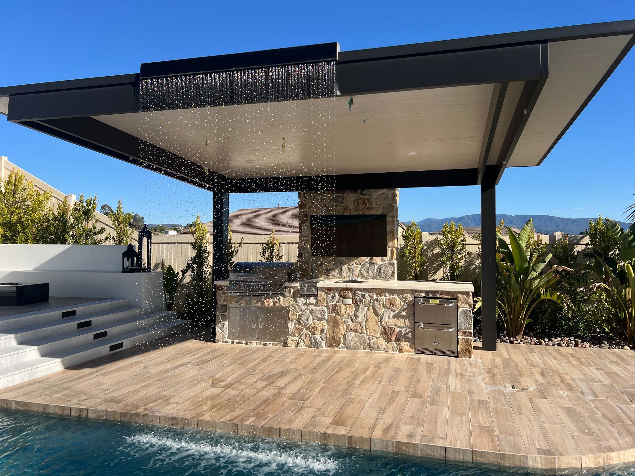 Covered outdoor kitchen with waterfall feature by the pool