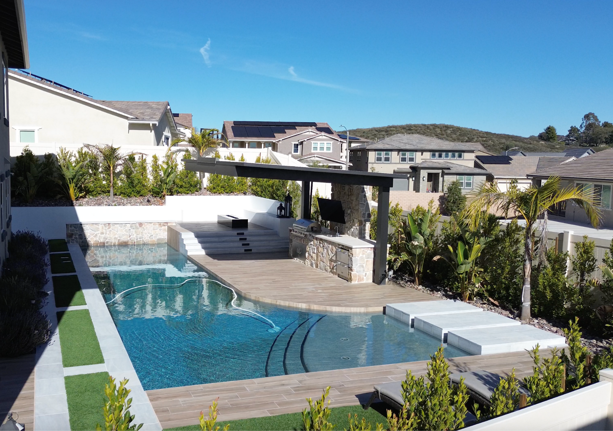Modern backyard pool with outdoor kitchen and palm landscaping