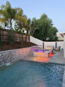 Illuminated raised spa with fire feature and stone wall.