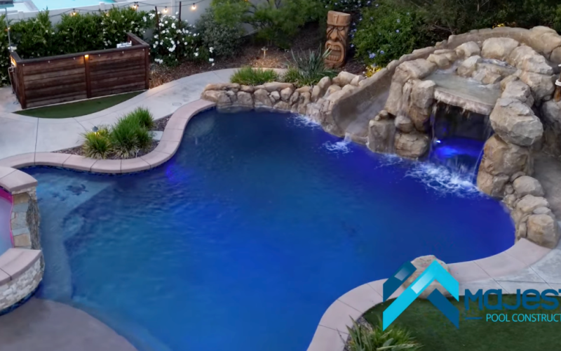 Custom freeform backyard pool in Southern California with rock waterfall, grotto, slide, spa, LED pool lighting, and travertine deck built by Majestic Pool Construction. representing freeform pools
